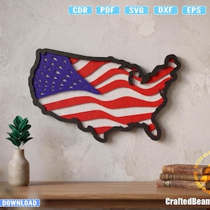 May include: A wooden wall hanging in the shape of the United States, featuring the American flag design. The flag has red and white stripes and a blue field with white stars. The piece is framed in black and mounted on a light-colored wall.