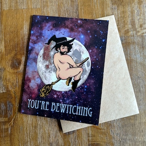 Könnte beinhalten: Grußkarte mit einer humorvollen Illustration einer Person, die auf einem Besen vor einem Vollmond und einem Sternenhimmel reitet. Der Text "YOU'RE BEWITCHING" ist darunter gedruckt. Inklusive einem leeren Kraftpapierumschlag.