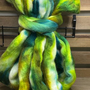 May include: A bundle of colorful fiber in shades of green, yellow, and white. The fiber is twisted and knotted, with a soft, textured appearance. The colors blend together, creating a vibrant and artistic look. Ideal for crafting projects.
