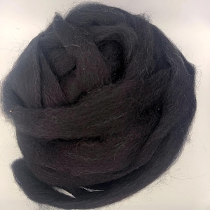 May include: A tightly wound ball of black wool roving. The wool appears soft and fluffy, with a slightly textured surface. The dark color suggests it could be used for various crafting projects, such as felting or spinning.