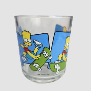May include: Clear glass tumbler with a cartoon image of Bart Simpson skateboarding. The design shows Bart in a red shirt and blue shorts, with a green skateboard against a blue background. The text "TM & © 2004 FOX" is printed on the glass.