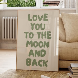 Può includere: Una stampa incorniciata con le parole "LOVE YOU TO THE MOON AND BACK" in lettere verdi. La stampa è esposta in una stanza con un divano beige, una pianta in vaso e una finestra.