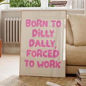 May include: A framed print with the text "BORN TO DILLY DALLY, FORCED TO WORK" in pink letters on a beige background. The print is displayed in a room with a window, a sofa, and a rug.
