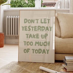 Puede incluir: Un póster motivacional enmarcado con fondo blanco y texto verde que dice "No dejes que ayer ocupe demasiado de hoy". El póster está apoyado en un sofá beige en un salón.