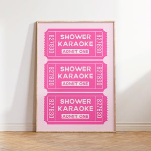 Puede incluir: Tres entradas rosas con el texto "Shower Karaoke" y "Admit One" impresas en ellas. Las entradas están enmarcadas en un marco de madera claro.