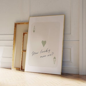 May include: A white framed print with a gold border featuring a stylized ace of hearts playing card with the text "How lucky are we?" in cursive.