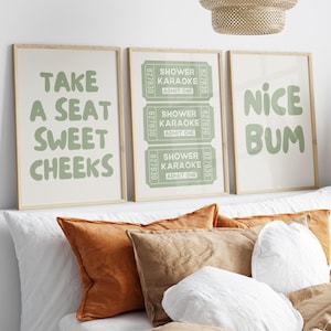 May include: Three framed art prints with light green text on a cream background. The prints read "TAKE A SEAT SWEET CHEEKS", "SHOWER KARAOKE ADMIT ONE", and "NICE BUM". The prints are displayed above a bed with pillows.