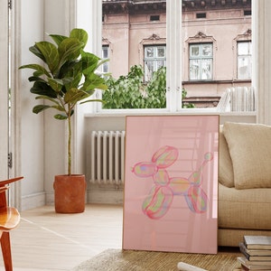 May include: A framed print of a colorful balloon animal shaped like a dog on a pink background. The print is hanging on a wall in a living room.