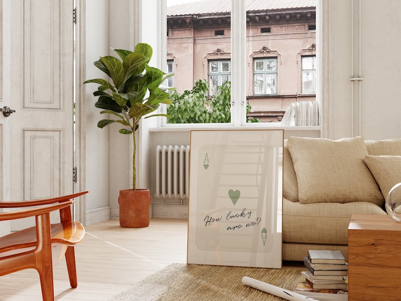 Puede incluir: Una impresi&oacute;n enmarcada de una carta de juego con un coraz&oacute;n verde y el texto "How lucky are we?" colgada en una pared blanca en una sala de estar. La impresi&oacute;n est&aacute; enmarcada en un marco dorado.