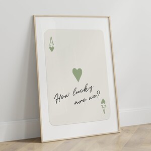 Puede incluir: Una impresi&oacute;n enmarcada de una carta de juego de as de corazones con un coraz&oacute;n verde y el texto "How lucky are we?" en escritura cursiva negra.