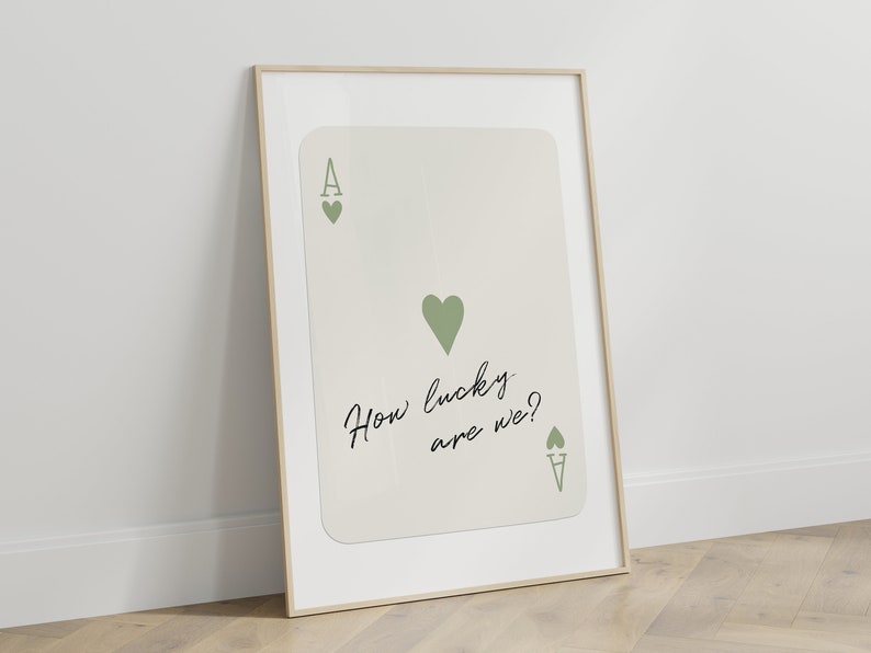 Puede incluir: Una impresi&oacute;n enmarcada de una carta de juego de as de corazones con un coraz&oacute;n verde y el texto "How lucky are we?" en escritura cursiva negra.