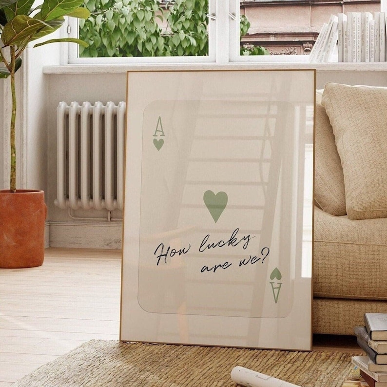 Puede incluir: Una impresi&oacute;n enmarcada con fondo blanco y un dise&ntilde;o de carta de juego de as de corazones verde. El texto "How lucky are we?" est&aacute; escrito en cursiva negra.