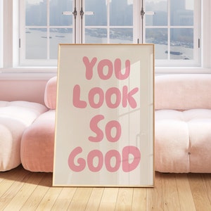 May include: A framed print with a pink background and the text "YOU LOOK SO GOOD" in large, pink, bubble letters.