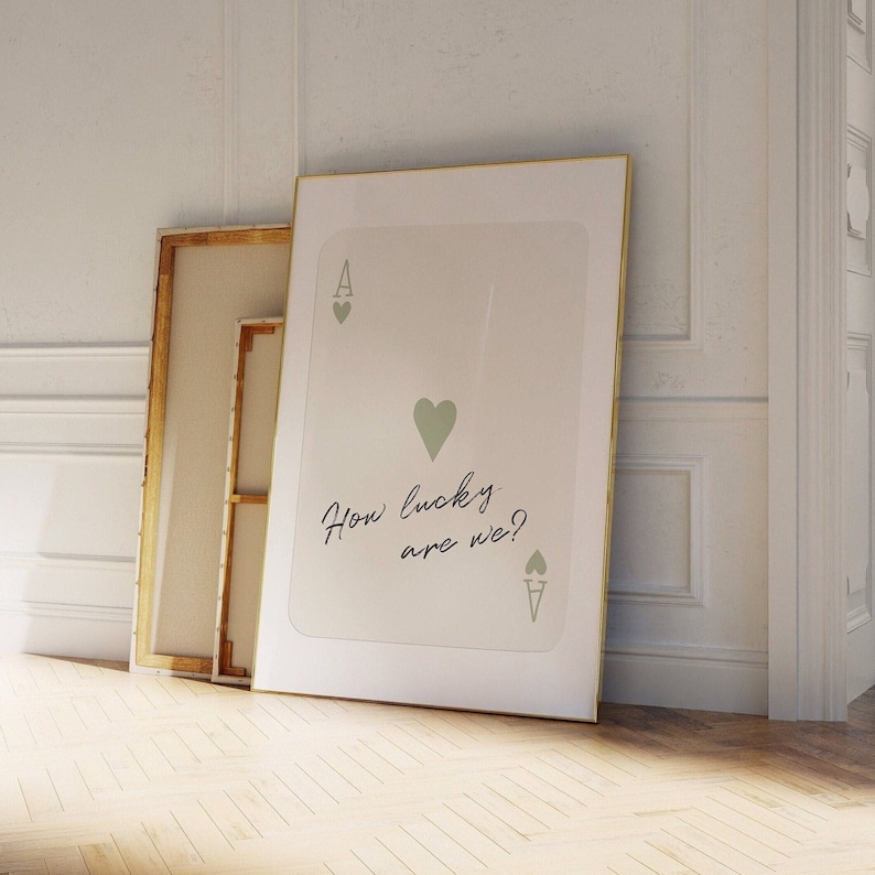 May include: A white framed print with a gold border featuring a stylized ace of hearts playing card with the text "How lucky are we?" in cursive.