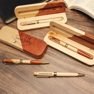 Könnte beinhalten: Holzstifte mit goldenen Akzenten und dem Text "Customization area" werden in offenen Holzboxen präsentiert. Eine Box trägt den Text "Hannah & James". Die Stifte haben eine helle Holzoberfläche mit dunklen Holzakzenten.