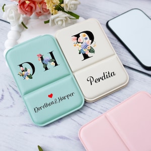 May include: Two personalized compact mirrors. One is mint green with the letters "DH" and the name "Dorothea & Harper". The other is off-white with the letter "P" and the name "Perdita". Both have floral designs.