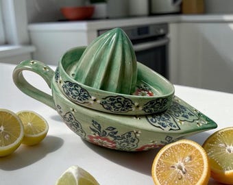 May include: A light green ceramic citrus juicer with a pointed reamer and a handle, decorated with a dark blue and red floral pattern. The juicer is surrounded by several halved and quartered yellow lemons on a white surface.