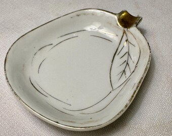 May include: White ceramic dish with a leaf design and gold trim. The dish has a pear shape with a gold accent at the top. The leaf design is outlined in gold. The dish is likely vintage.