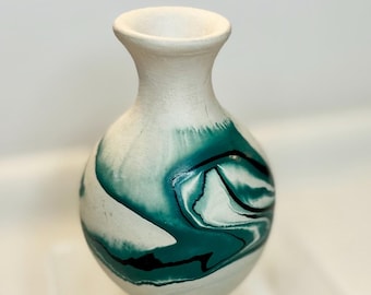 Könnte beinhalten: Eine weiße Keramikvase mit einem türkis-schwarzen Marmormuster. Die Vase hat einen abgerundeten Körper und einen schmalen Hals. Die türkisfarbene Farbe wirbelt um die Vase und erzeugt ein einzigartiges Muster. Glatte, matte Oberfläche.