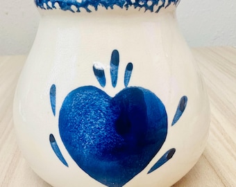 Könnte beinhalten: Ein cremefarbener Keramiktopf mit bauchigem Körper und ausgestelltem Rand. Die Außenseite ist mit einem handgemalten, dunkelblauen Herz in der Mitte verziert, das von kleinen blauen tropfenförmigen Akzenten und einem gesprenkelten Rand umgeben ist.
