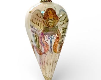 May include: A teardrop-shaped Christmas ornament featuring a hand-painted angel design. The angel has brown hair, a halo, and detailed wings. The ornament is primarily cream-colored with gold accents and a gold cap for hanging.