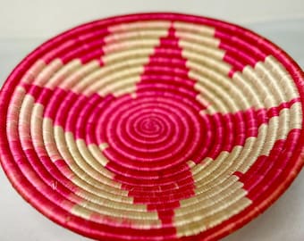Könnte beinhalten: Ein runder, gewebter Korb mit einem Spiralmuster in der Mitte. Der Korb hat abwechselnde Bänder aus leuchtendem Pink und Beige. Der äußere Rand ist ein durchgehendes pinkfarbenes Band. Dieser dekorative Korb eignet sich für die Inneneinrichtung.