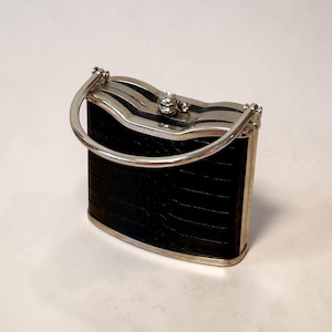 May include: A small, vintage black handbag with a silver-toned frame and handle. The bag features a textured, possibly leather, exterior and a decorative clasp with a small, clear gem. The handle is a curved, silver bar.