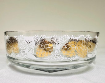 May include: Clear glass bowl with a gold rim and a decorative pattern of gold pinecones and white branches. The bowl has a wide, shallow shape and a triangular base. The design is repeated around the bowl's exterior.
