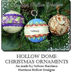 May include: Three handmade hollow dome Christmas ornaments. One is white with purple flowers and a purple ribbon, one is blue with red and white flowers and a white ribbon, and one is brown with a swirling pattern. The blue ornament has the word "Name" written on it.