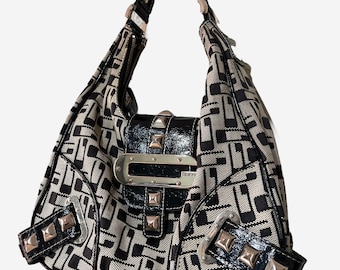 May include: A black and white patterned shoulder bag with a black strap. The bag features a silver buckle and studded accents. The brand name "GUESS" is visible on the front.