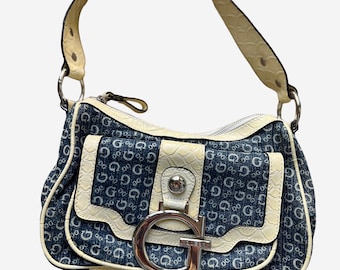 May include: A denim-style handbag with a cream-coloured handle and trim. The bag features a large silver-tone "G" logo on the front and a zip closure. The bag's design includes a repeating "G" pattern.