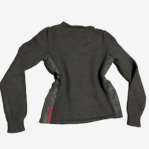 Puede incluir: Suéter gris oscuro con mangas y espalda de punto acanalado. Los laterales presentan un material acolchado verde oliva con un detalle de raya roja. El suéter tiene cuello redondo y puños acanalados.