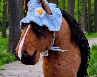 May include: A brown and white stuffed horse head with a blue crocheted hat with a white daisy on top. The horse has a black mane and tail.