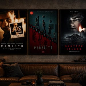 May include: Three framed film posters, including "Memento", "Parasite", and "Shutter Island", are displayed above a brown leather sofa. The "Memento" poster features a man's face and a polaroid. The "Parasite" poster has a red and teal colour scheme. The "Shutter Island" poster shows a man's face and an island.