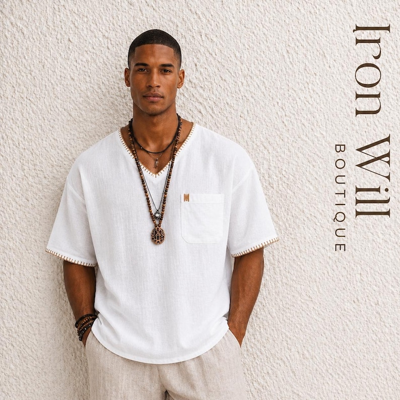 May include: A white linen V-neck shirt with a chest pocket and tan trim. The shirt is paired with tan pants and layered beaded necklaces. The image includes the text "Iron Will Boutique".