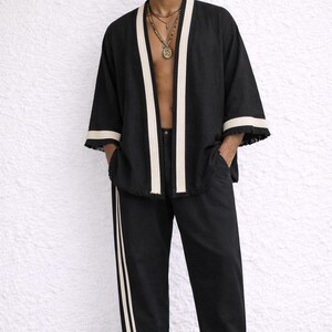 Puede incluir: Chaqueta estilo kimono negra con ribete color crema y pantal&oacute;n a juego. La chaqueta tiene mangas anchas y flecos. El pantal&oacute;n tiene una raya color crema en el lateral. El conjunto se combina con zapatillas blancas.