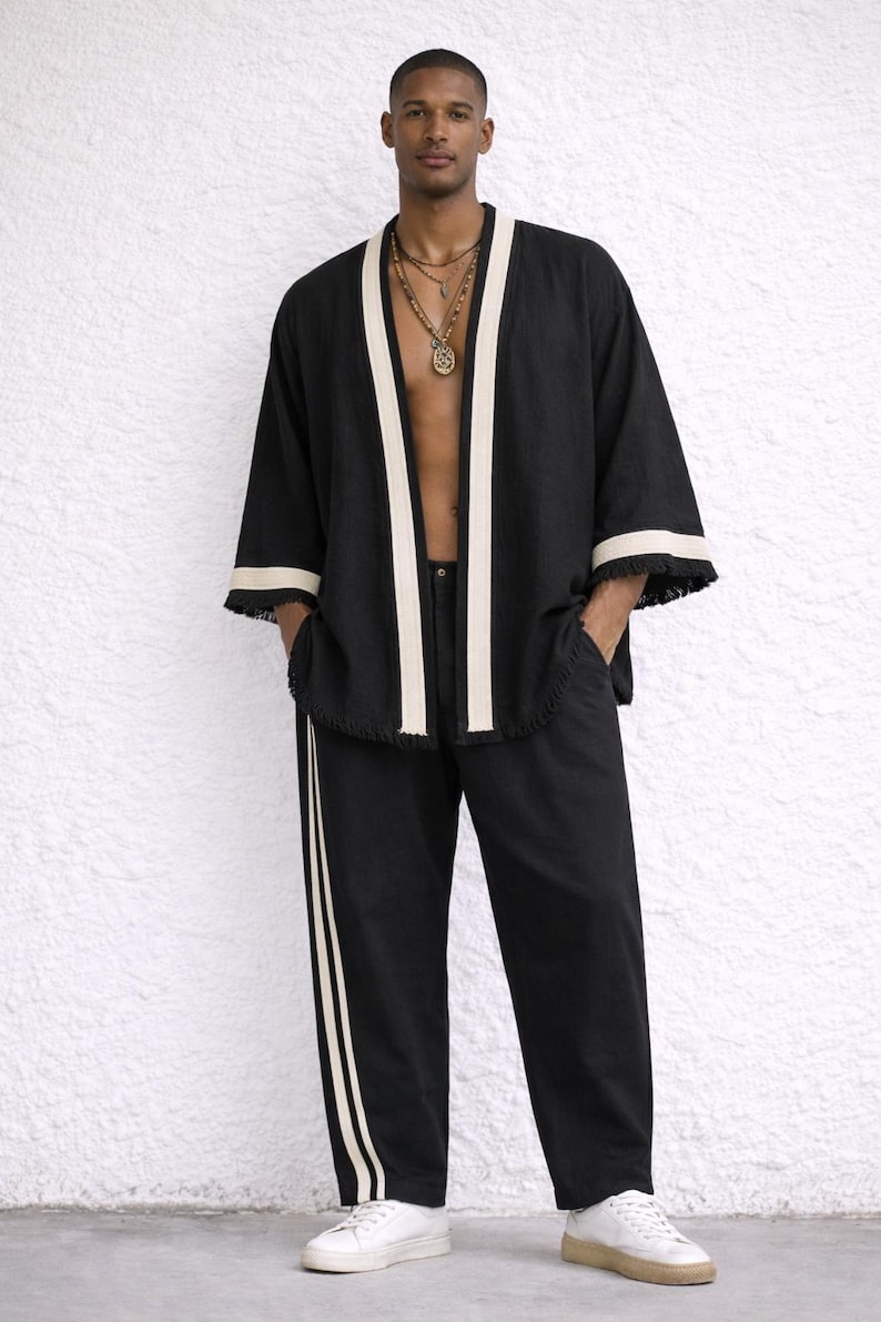 Puede incluir: Chaqueta estilo kimono negra con ribete color crema y pantal&oacute;n a juego. La chaqueta tiene mangas anchas y flecos. El pantal&oacute;n tiene una raya color crema en el lateral. El conjunto se combina con zapatillas blancas.