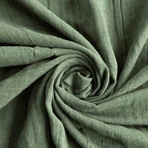 May include: Close-up of sage green fabric with a textured, slightly wrinkled appearance. The fabric is arranged in a swirling pattern, creating a sense of depth and movement. The color is a muted, earthy green.