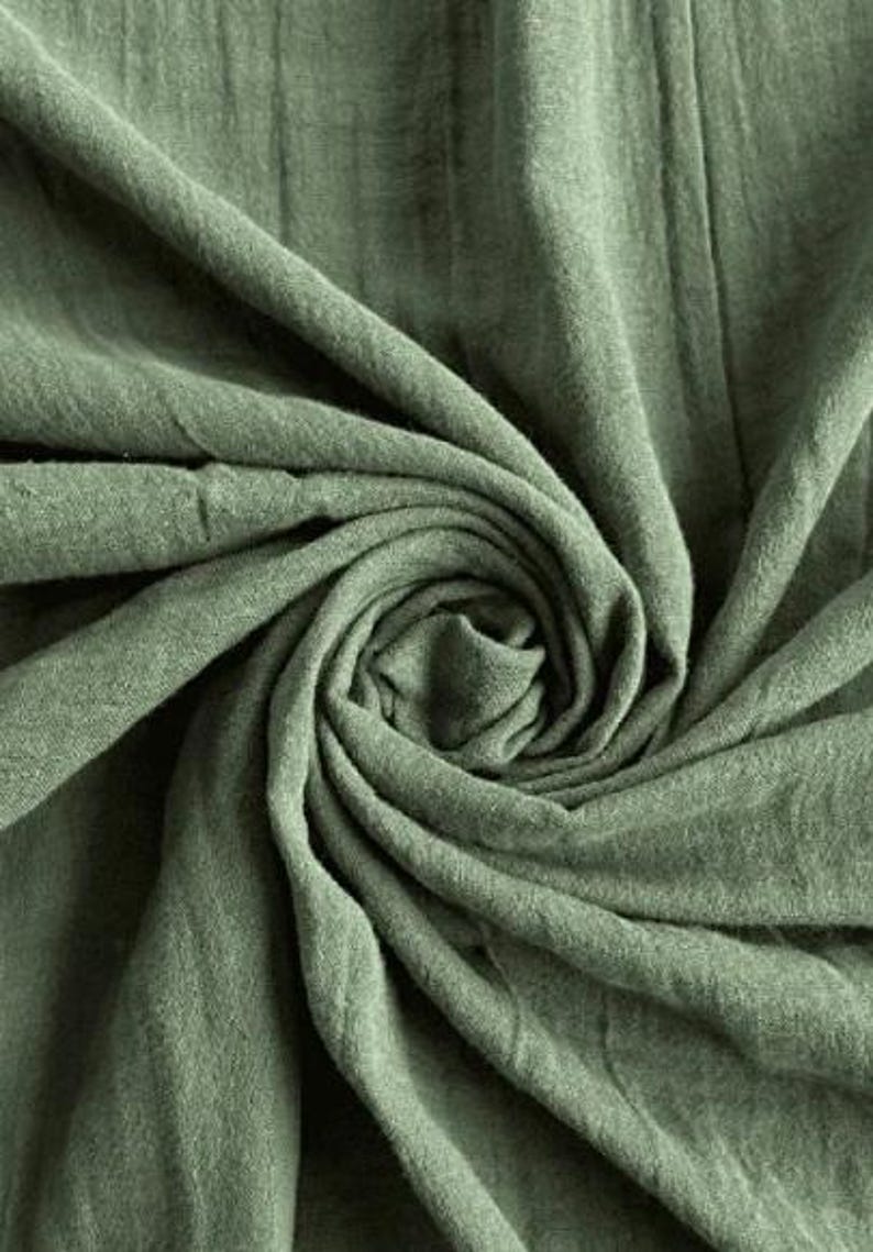 May include: Close-up of sage green fabric with a textured, slightly wrinkled appearance. The fabric is arranged in a swirling pattern, creating a sense of depth and movement. The color is a muted, earthy green.