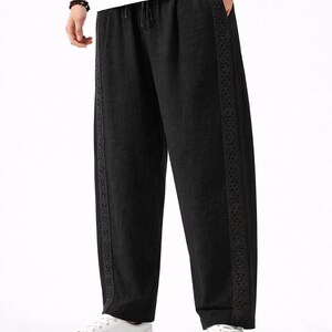 May include: Black linen pants with a drawstring waist and decorative trim along the sides. The pants are loose-fitting and paired with white sneakers. The overall style is casual and comfortable.