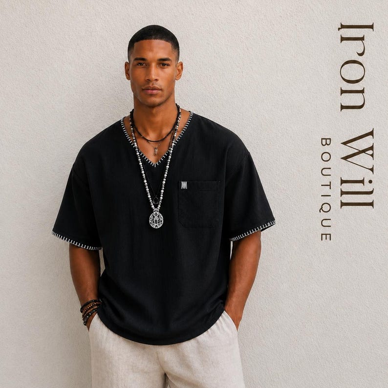 May include: Black V-neck shirt with white stitching on the collar and sleeves. The shirt has a pocket on the chest and a small logo. The model is wearing multiple necklaces and bracelets. The text "Iron Will Boutique" is on the right side.