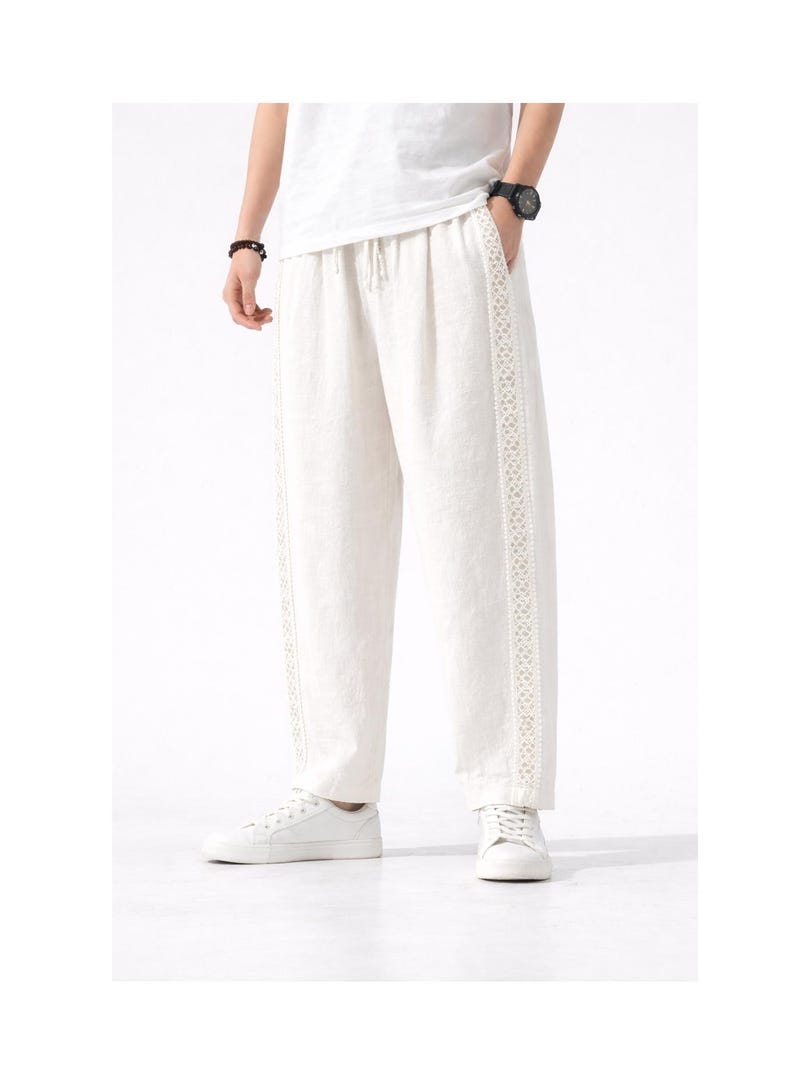 May include: Off-white linen pants with a drawstring waist and decorative trim along the side seams. The pants are paired with white sneakers. The style is casual and comfortable.