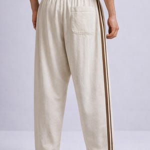 Puede incluir: Pantalones de lino beige con una raya marr&oacute;n en el lateral. Los pantalones tienen un corte holgado, un bolsillo trasero y cintura con cord&oacute;n. Se combinan con zapatillas blancas.