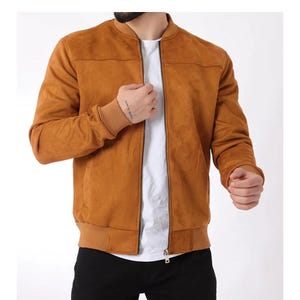 Puede incluir: Una chaqueta tipo bomber de color tostado con una textura suave similar al ante, que presenta cuello, puños y dobladillo acanalados. La chaqueta tiene un cierre de cremallera central plateado, mangas largas y un diseño liso sobre una camiseta.