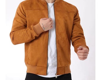 Peut inclure: Un blouson bomber en daim beige doté d'un col, de poignets et d'un ourlet côtelés, avec une fermeture éclair frontale intégrale. La veste est portée sur un t-shirt blanc uni et associée à un pantalon noir, offrant un design épuré.