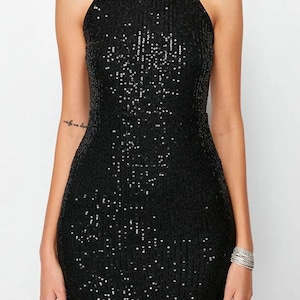 May include: A black sequin halter dress. The dress is sleeveless and has a fitted silhouette. The sequins catch the light, creating a shimmering effect. The dress is a mini length and is suitable for a party or special occasion.