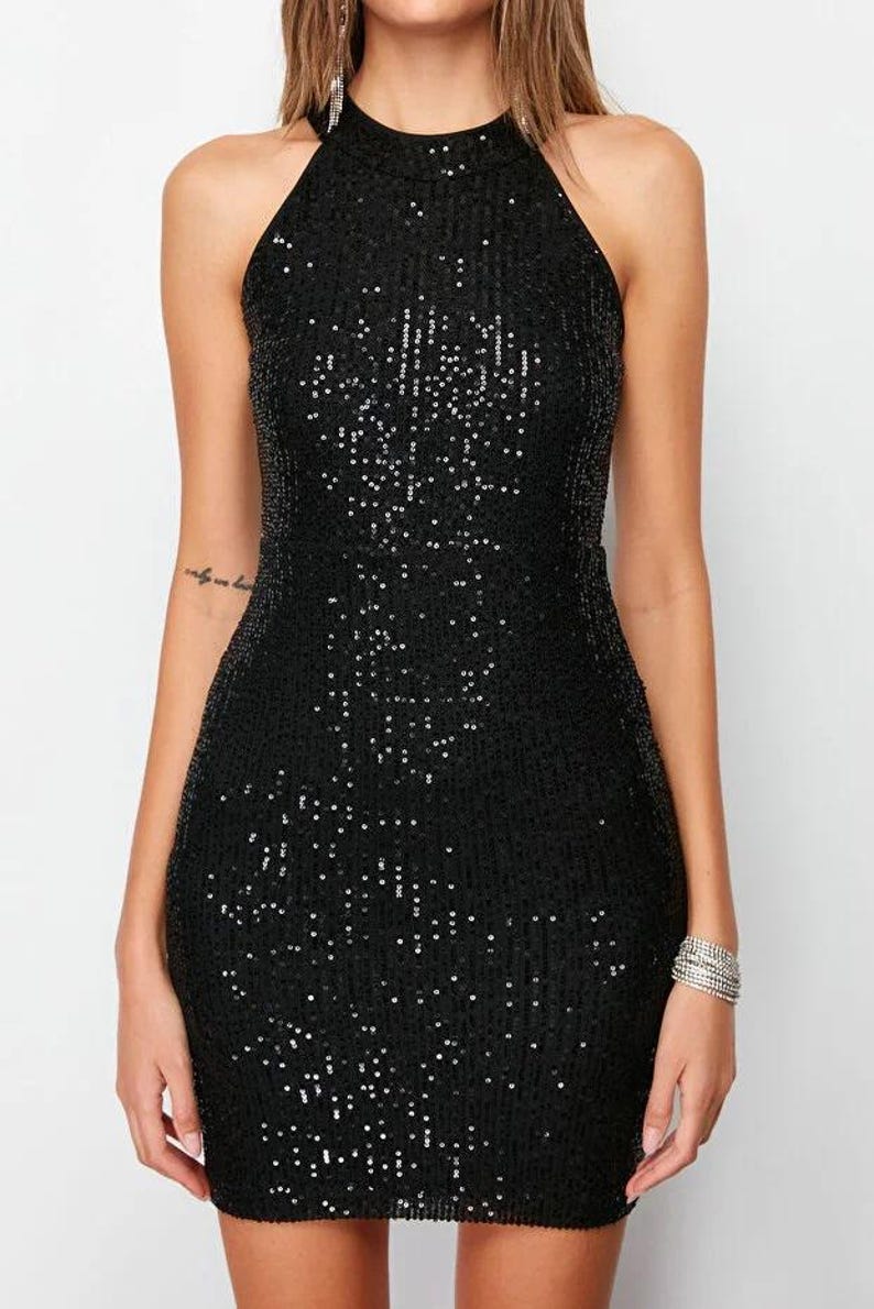 May include: A black sequin halter dress. The dress is sleeveless and has a fitted silhouette. The sequins catch the light, creating a shimmering effect. The dress is a mini length and is suitable for a party or special occasion.