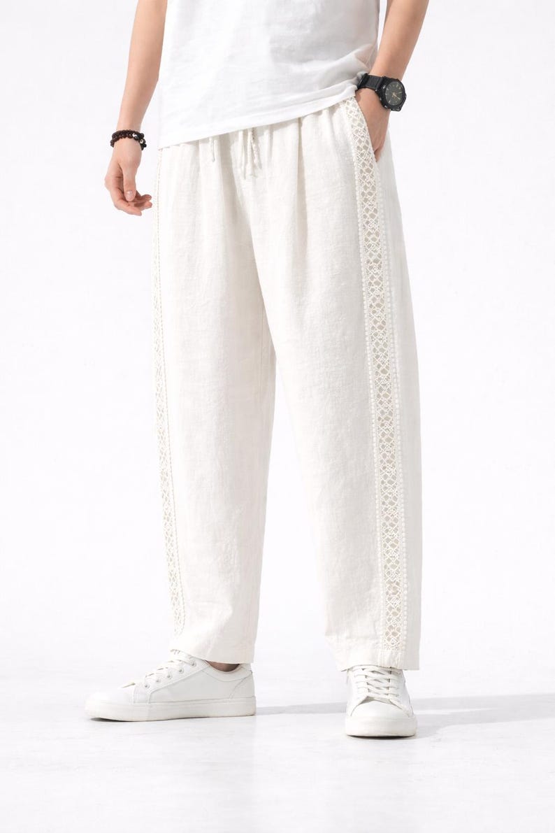 May include: Off-white linen pants with a drawstring waist and decorative lace trim down the sides. The pants are paired with white sneakers and a white t-shirt. The overall style is casual and comfortable.