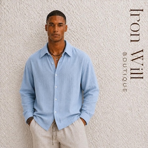 May include: A pale blue long-sleeved shirt with a button-down design. The shirt is worn with light-coloured trousers. The text "Iron Will Boutique" is displayed vertically on the right side of the image.