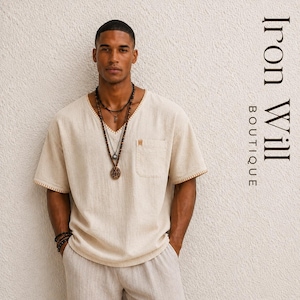 May include: A beige V-neck short-sleeve shirt with a pocket and decorative stitching. The shirt is paired with matching pants and layered necklaces. The text "Iron Will Boutique" is visible on the right side.